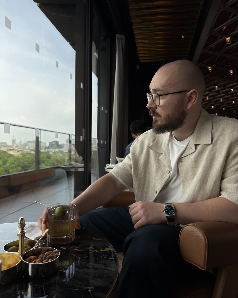Rooftop bar table with a drink and olives, the London skyline beyond